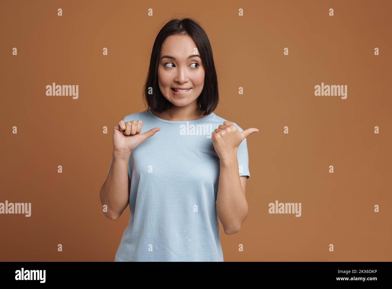Lip Pointing Young asian woman biting her lip and pointing fingers aside isolated ...