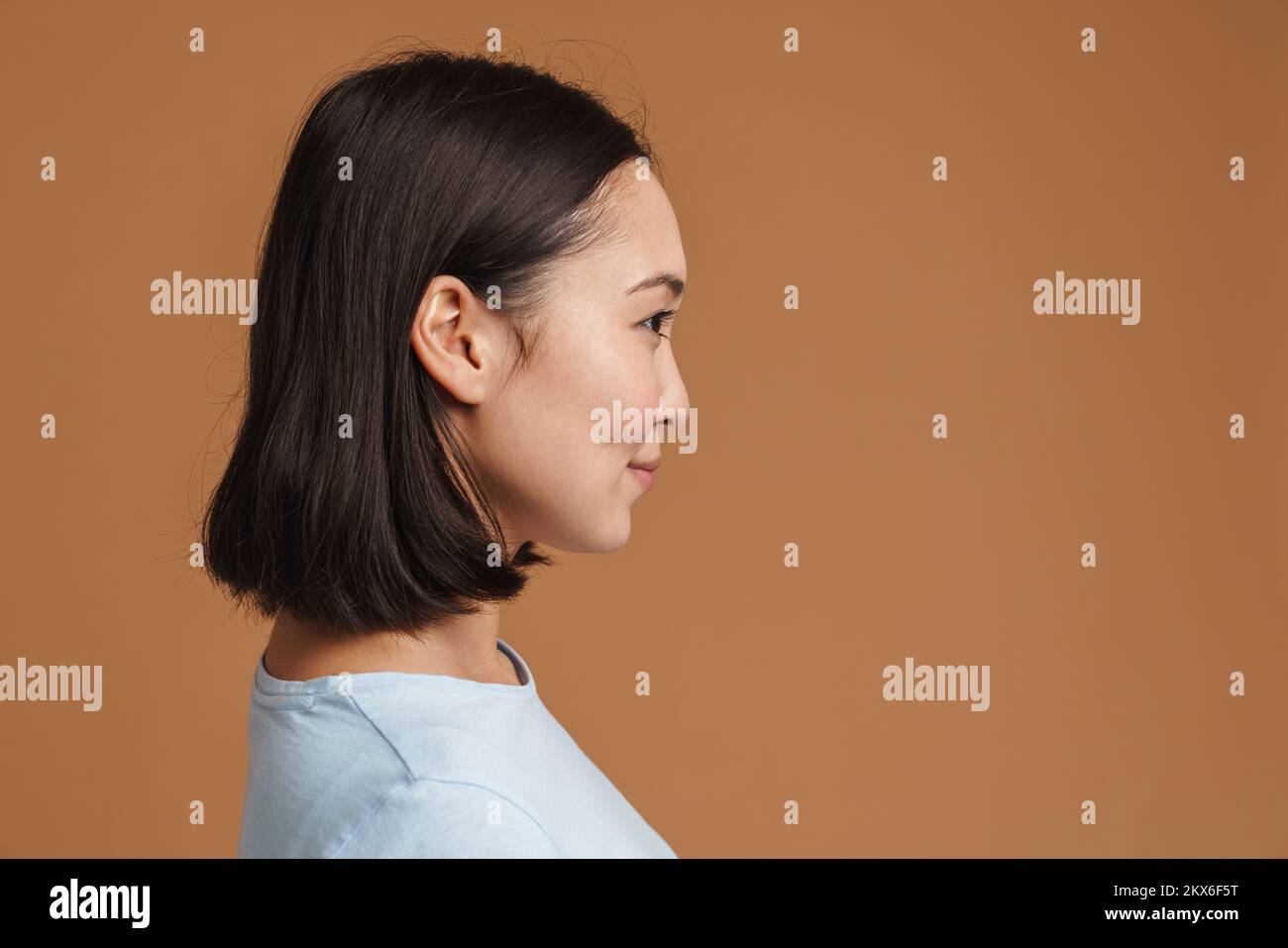 Young asian woman smiling while posing in profile isolated over beige ...