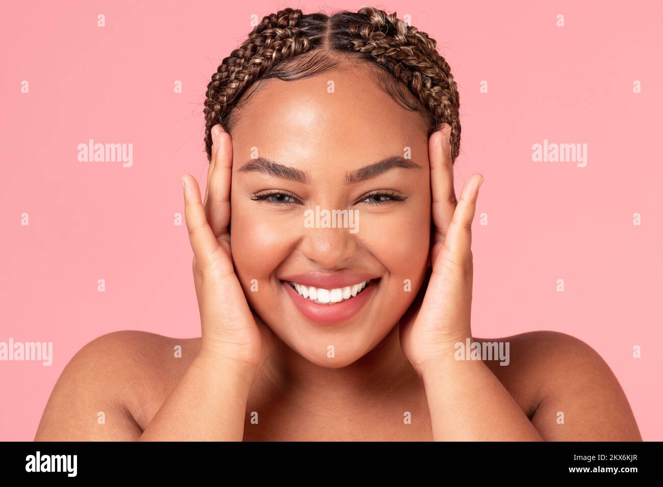 Portrait of happy beautiful african american woman touching her face and smiling at camera, posing over pink background Stock Photo
