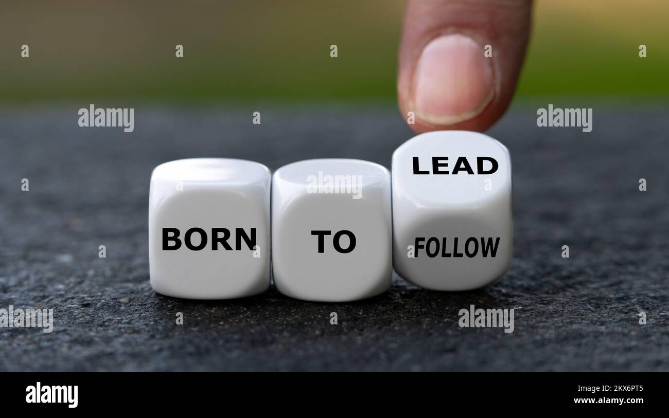 Hand turns dice and changes the expression 'born to follow' to 'born to lead'. Stock Photo