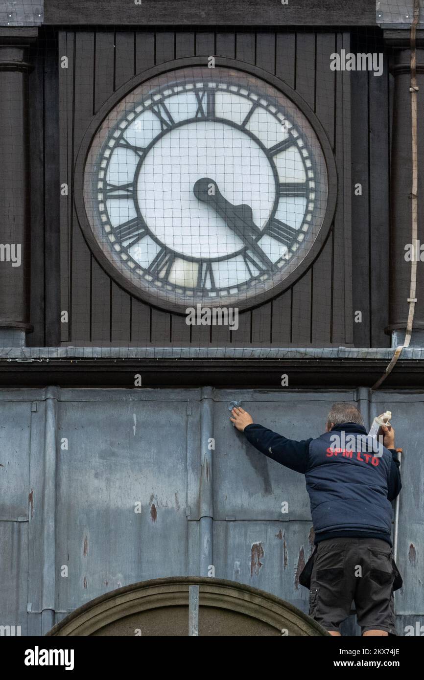 Person up a ladder cleaning lead cladding on a clock tower wtih