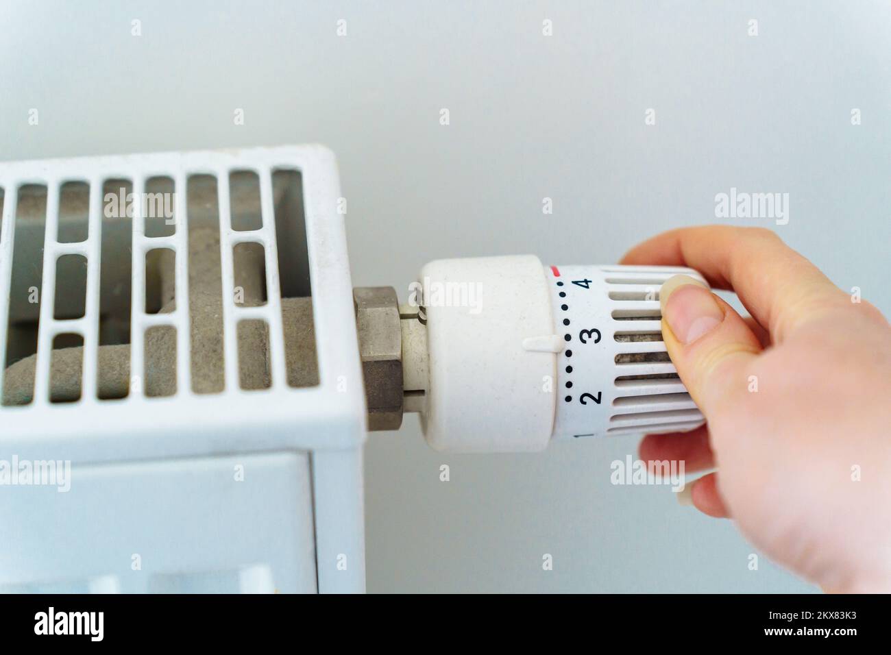 A hand turns the regulator on the heating radiator of the house. The concept of saving resources and heat energy in connection with the energy crisis Stock Photo