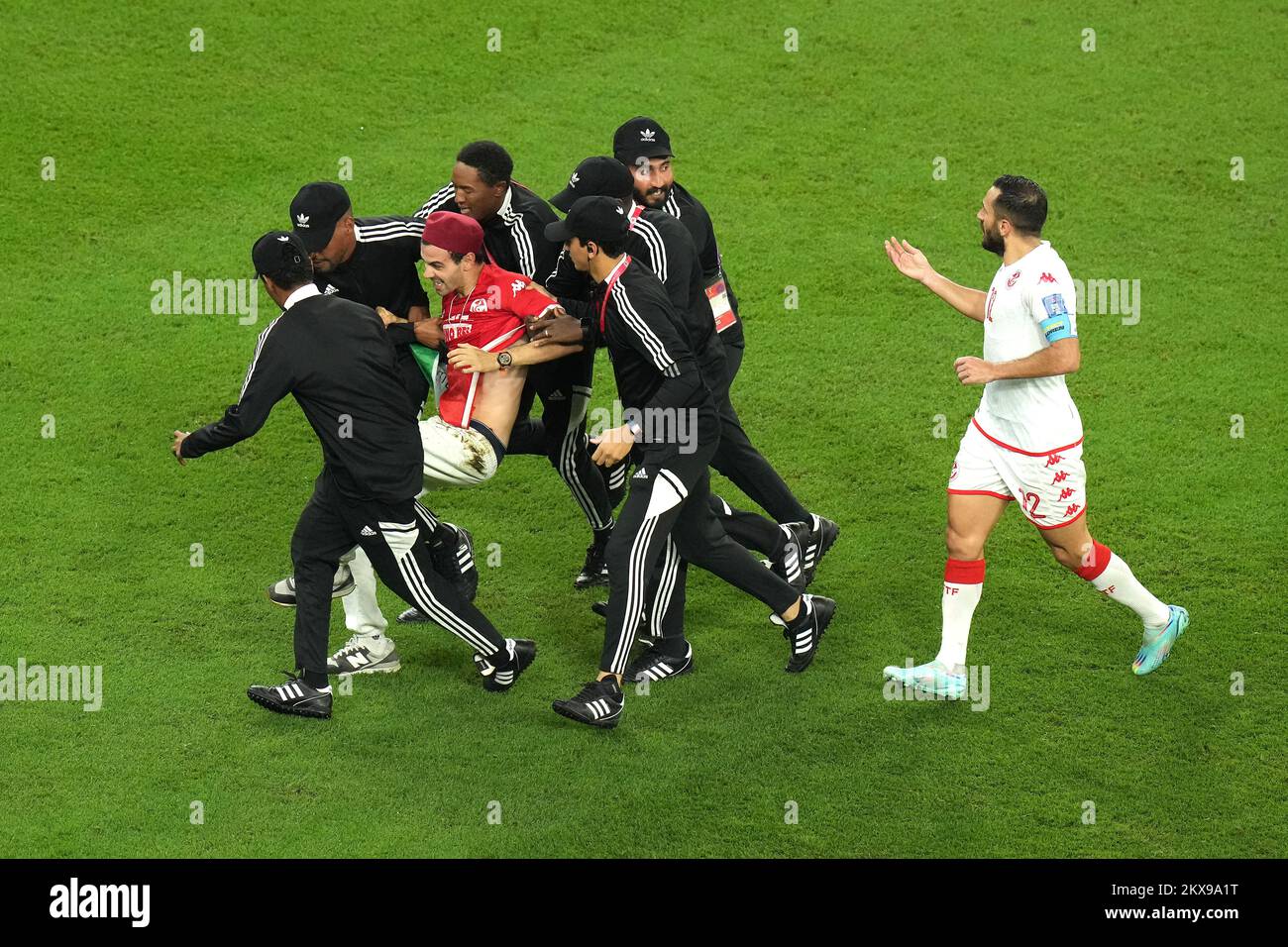 A pitch invader is escorted off the pitch as Tunisia's Ali Maaloul (right) speaks to security during the FIFA World Cup Group D match at the Education City Stadium in Al Rayyan, Qatar. Picture date: Wednesday November 30, 2022. Stock Photo