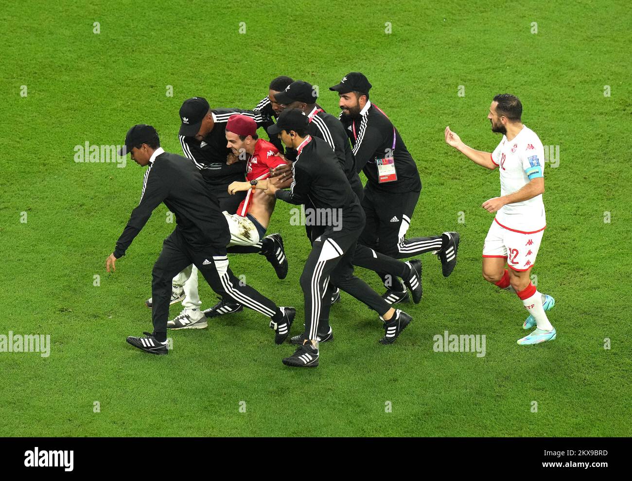 A pitch invader is escorted off the pitch as Tunisia's Ali Maaloul (right) speaks to security during the FIFA World Cup Group D match at the Education City Stadium in Al Rayyan, Qatar. Picture date: Wednesday November 30, 2022. Stock Photo