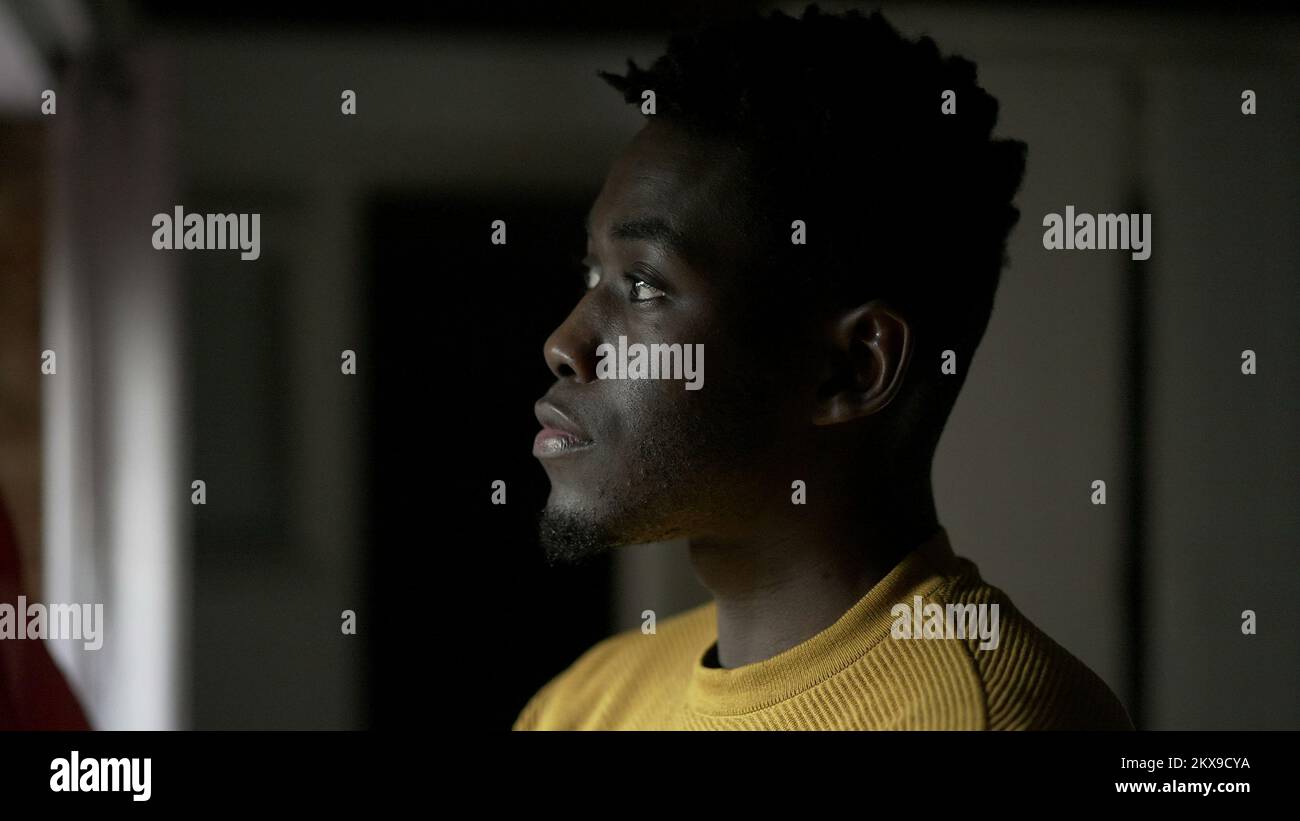 Pensive black African man standing by window, close-up face thinking Stock Photo