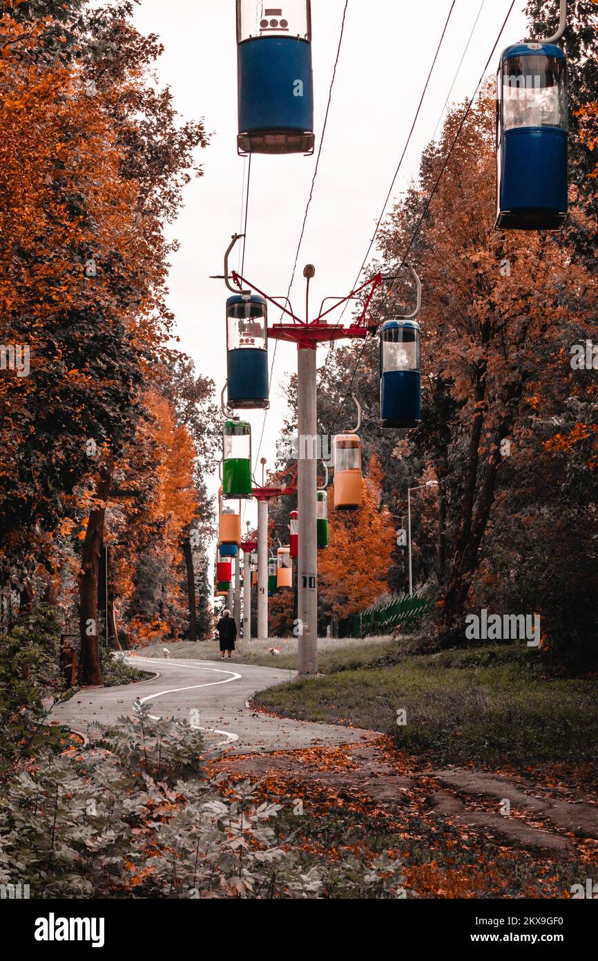 Colorful cableway cabins in autumn city park with golden trees and gray sky. Color graded Stock Photo