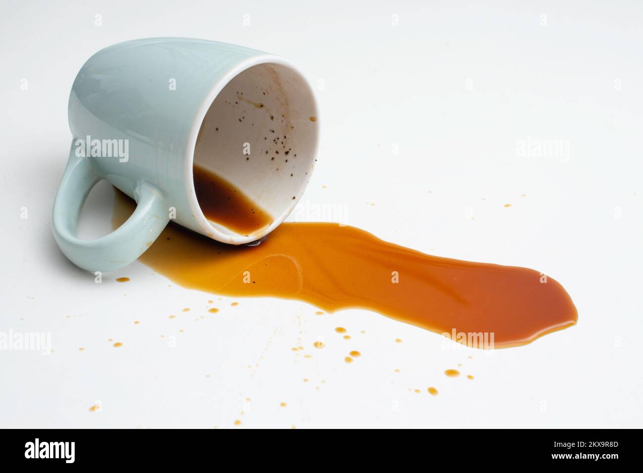 Coffee spill from a blue cup on white background, soft focus close up