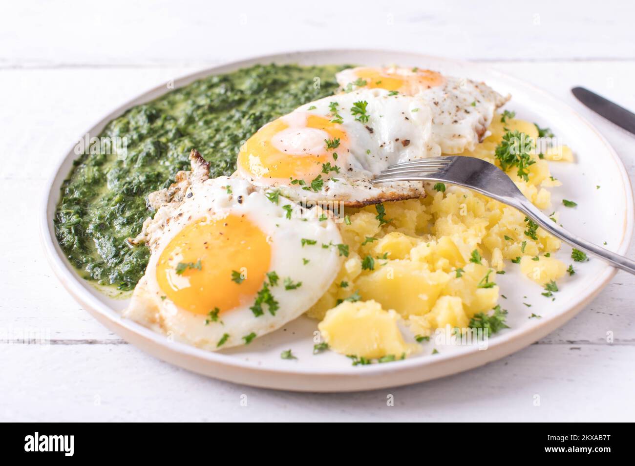 Creamed spinach with fried eggs, sunny side up and boiled potatoes on a plate isolated on white background Stock Photo