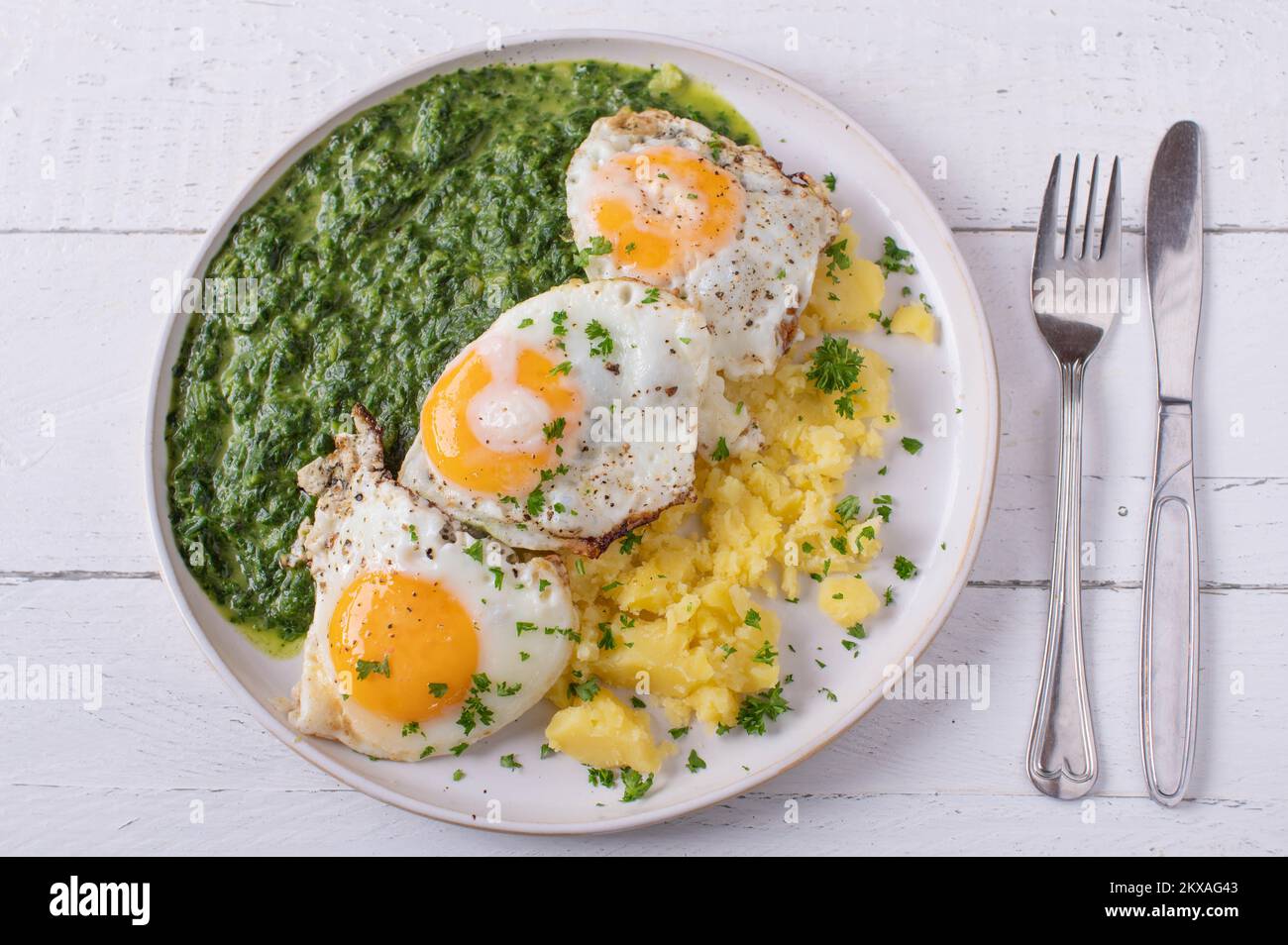 Creamed spinach with fried eggs and potatoes on a plate isolated on ...