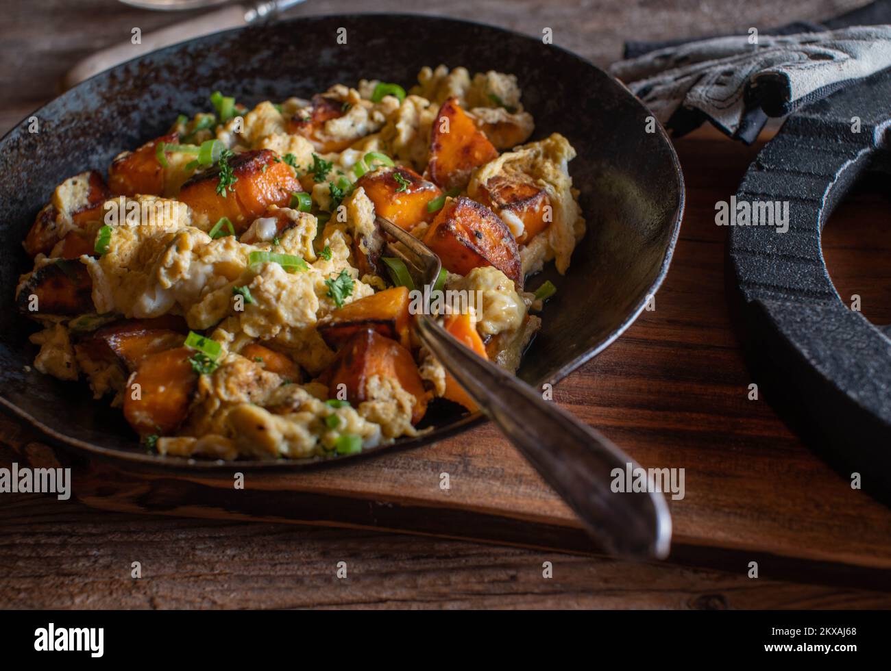 Roasted sweet potatoes with scrambled eggs, chives and parsley in a rustic pan. Healthy muscle