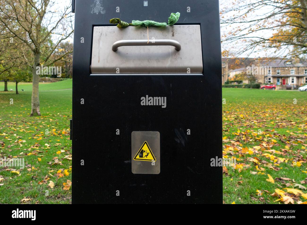 Close up of a large dog poo bin in a park in Ikley with an amusing sign about banging you head. UK Stock Photo