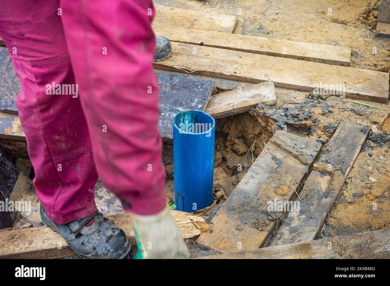 a worker standing next to the plastic water pipe sticking out of the
