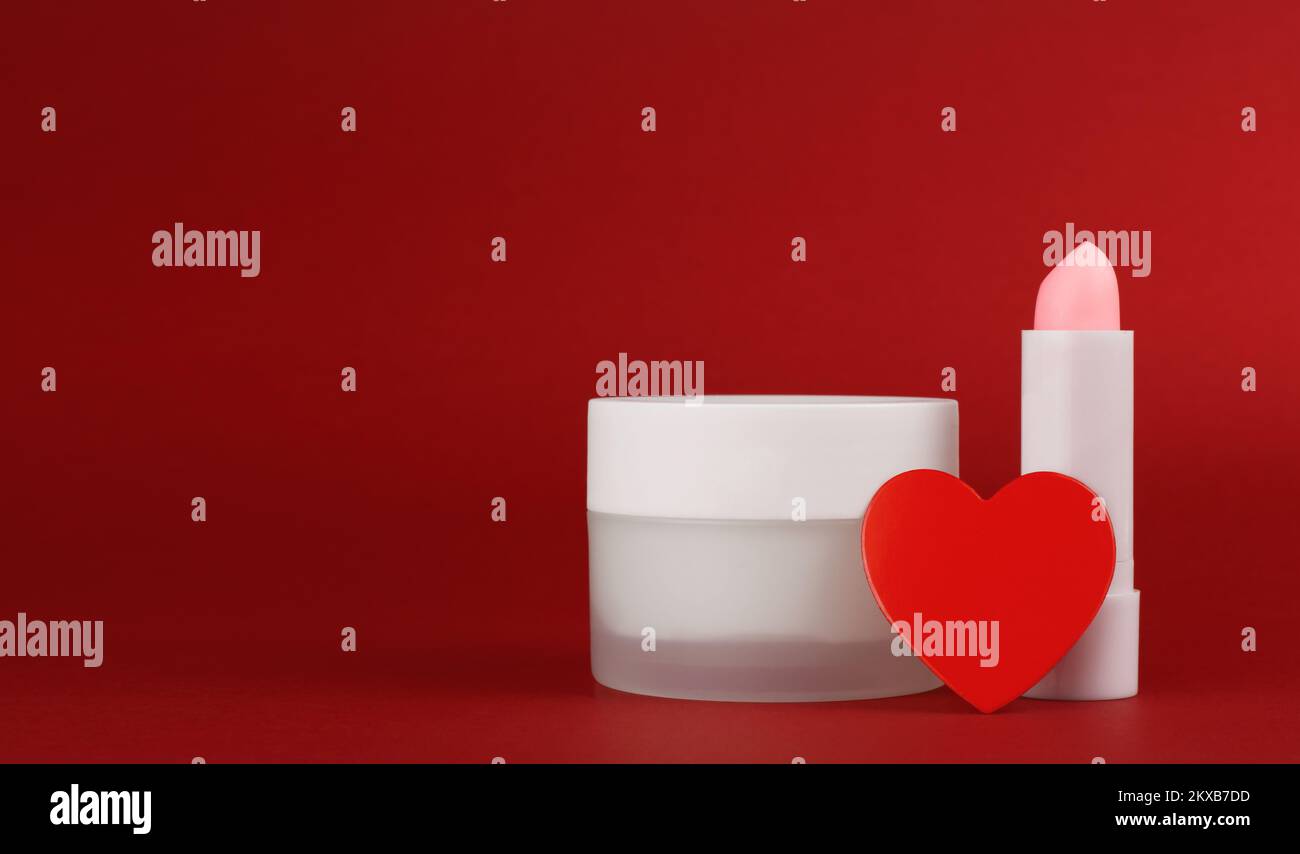 Jar of cream and lip balm on a red background with heart. Container for body care balm. Concept background for Valentine's Day. Blank advertisement wi Stock Photo