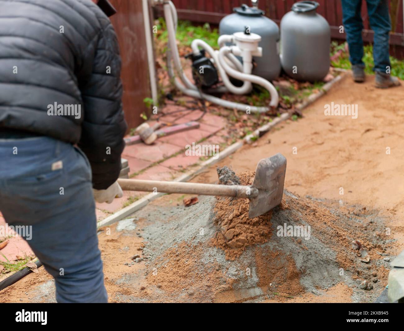 a worker mixing sand and cement to arrange an area around outdoor pool