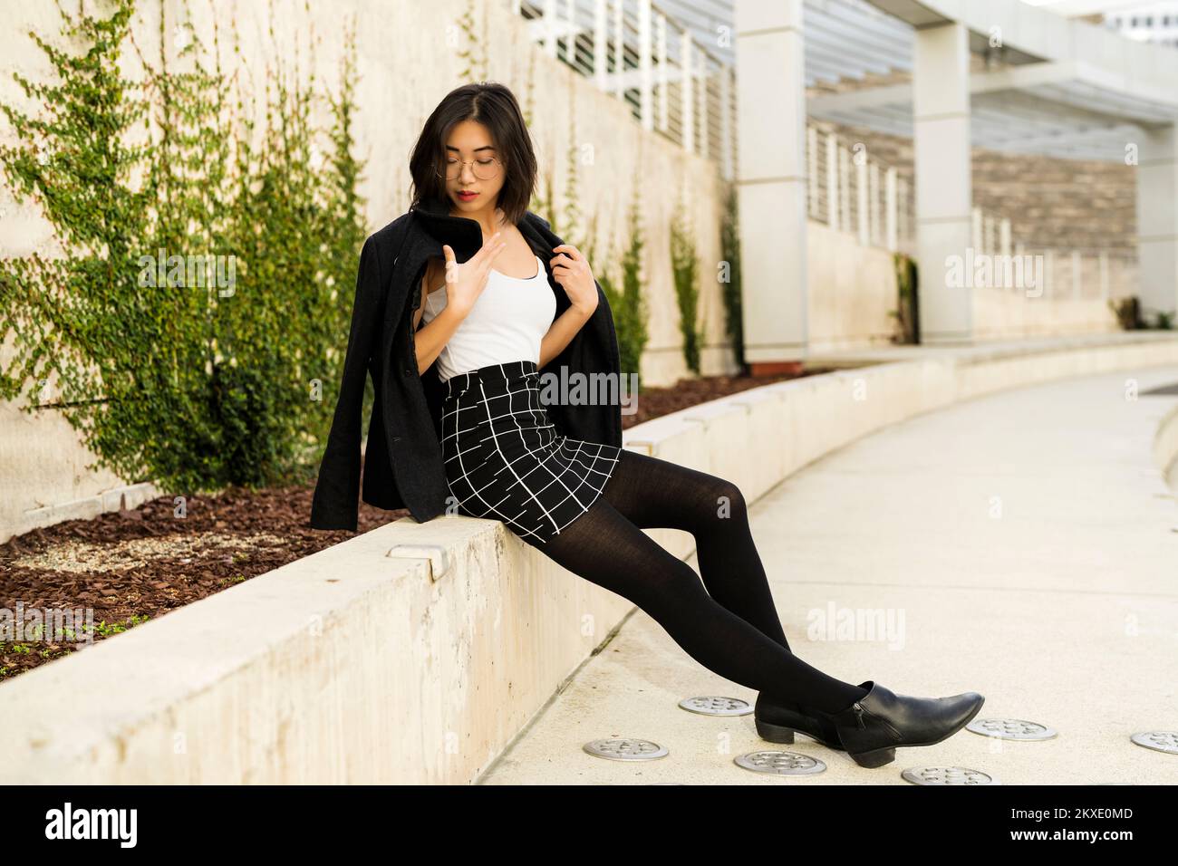 Side View of Young Woman Wearing Business Casual Attire Seated Outside at San Jose City Hall Stock Photo