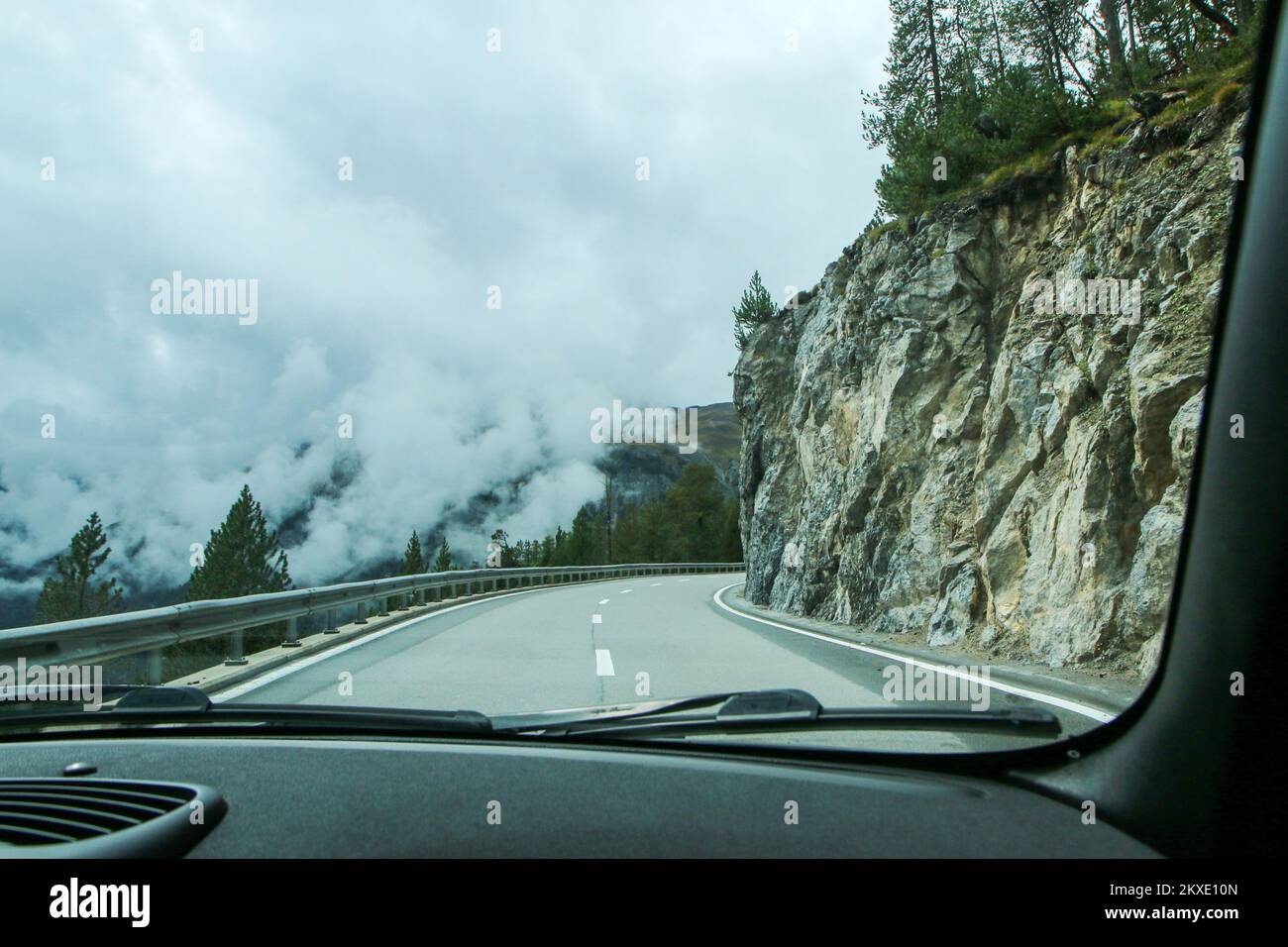 Driving the car on the alpine roads during the summer cloudy and rainy day. The peaks are in the clouds, the roads are tricky. Stock Photo