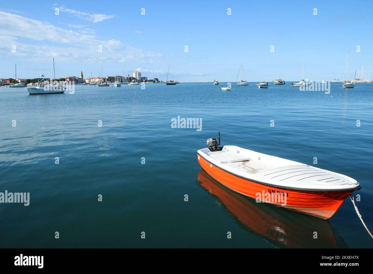 The calm bay with one orange boat at the harbor of the Croatian city of Umag. Nice sunny day in this vacation tourist target. Stock Photo