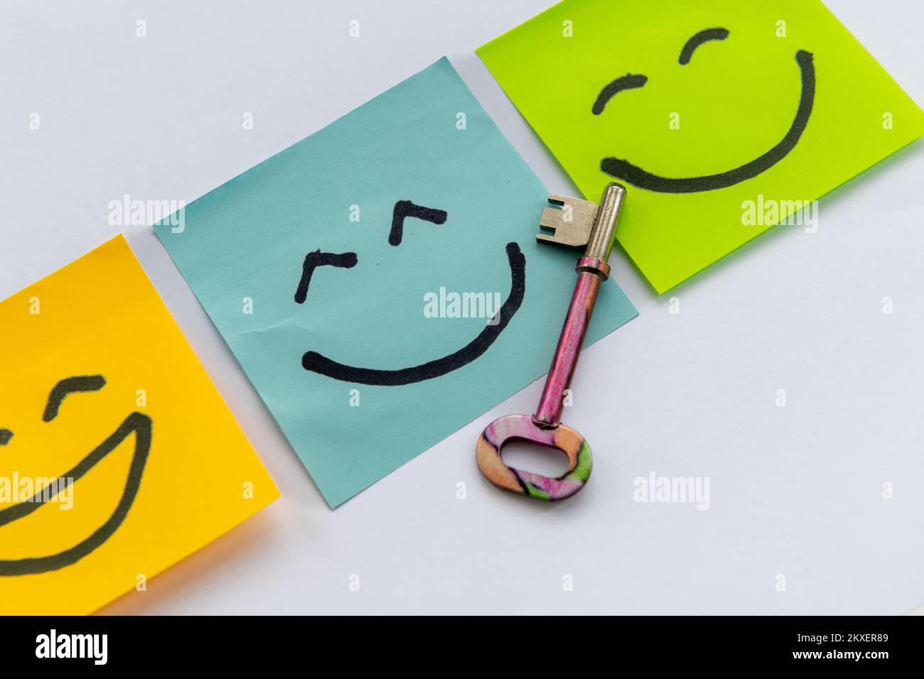A key to happiness concept with a key and hand drawn happy faces isolated in a white background. Stock Photo