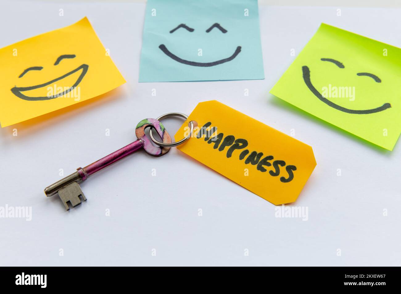A key to happiness concept with a key and hand drawn happy faces isolated in a white background. Stock Photo