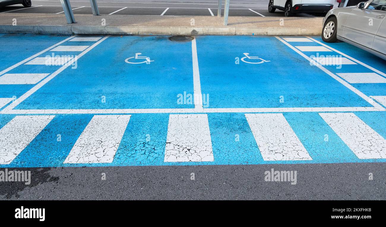 Double free parking space reserved for the disabled on blue asphalt with the international handicap symbol painted in white with the bright blue of Stock Photo