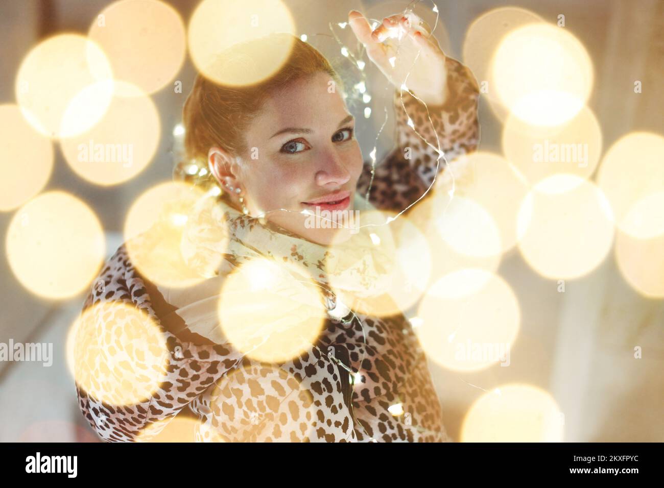 Young 30s redhead woman holding LED garland light outdoors looking back Stock Photo