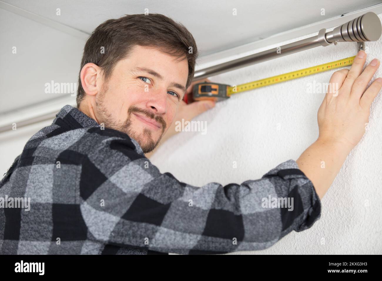 man measuring under a curtain rail Stock Photo
