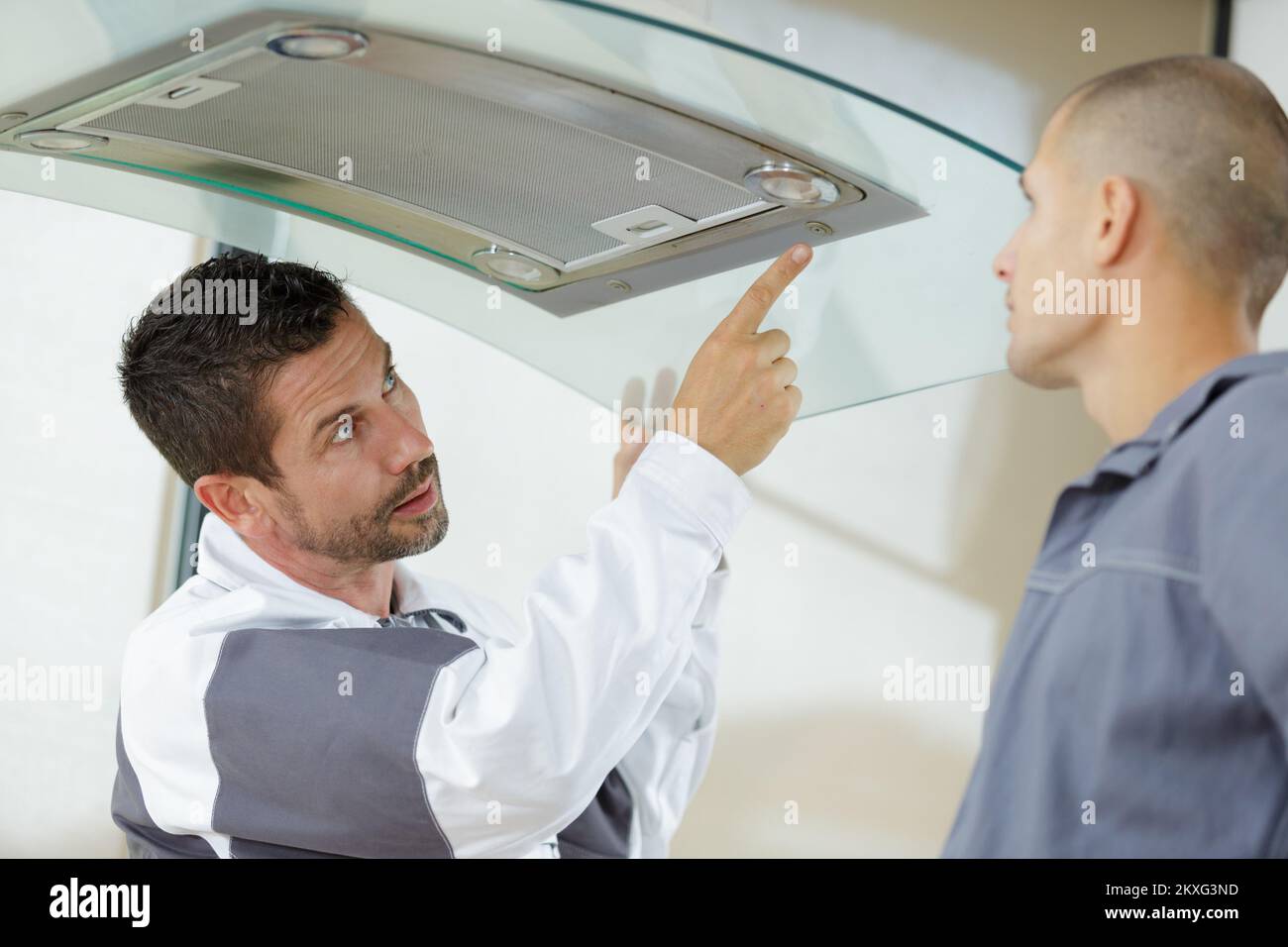mentor and young male repairman checking kitchen extractor filter Stock Photo