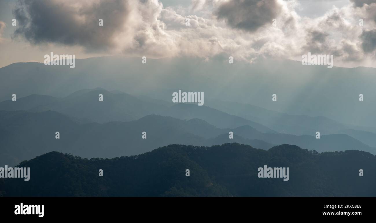 Mountain landscape with bright sun rays shining and cloudy sky in the morning. Stock Photo
