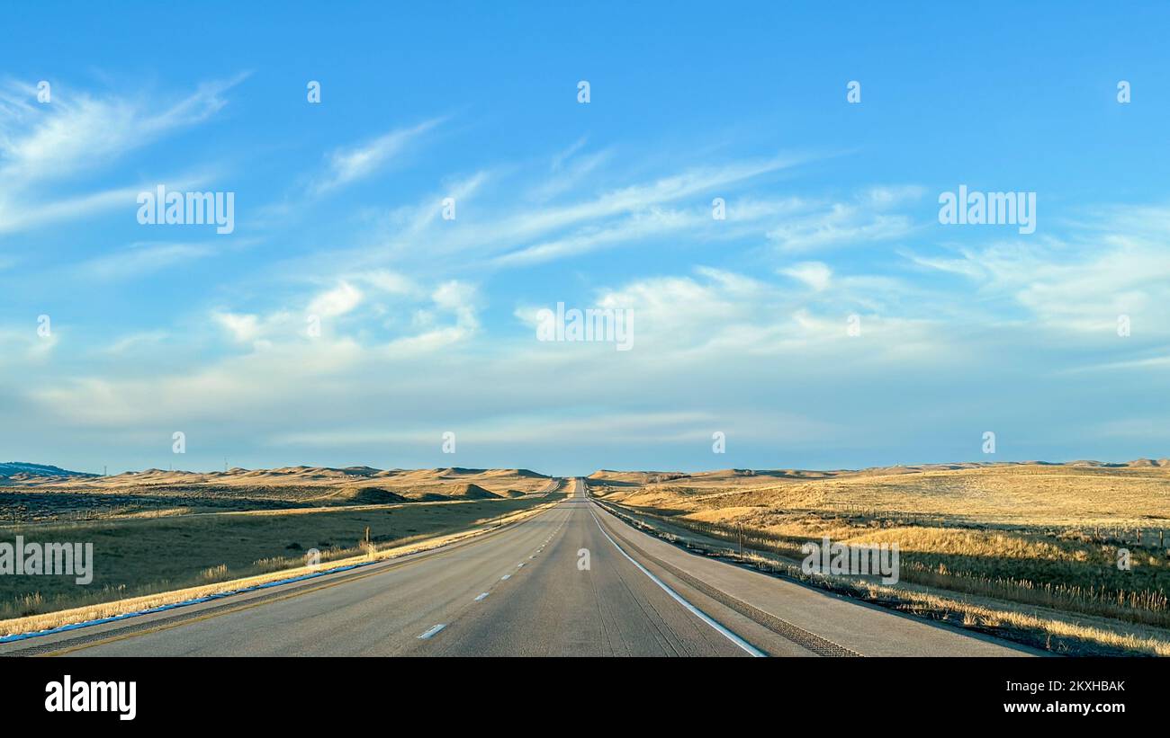 Deserted highway in Wyoming with wide, open spaces and blue cloudy skies. Stock Photo
