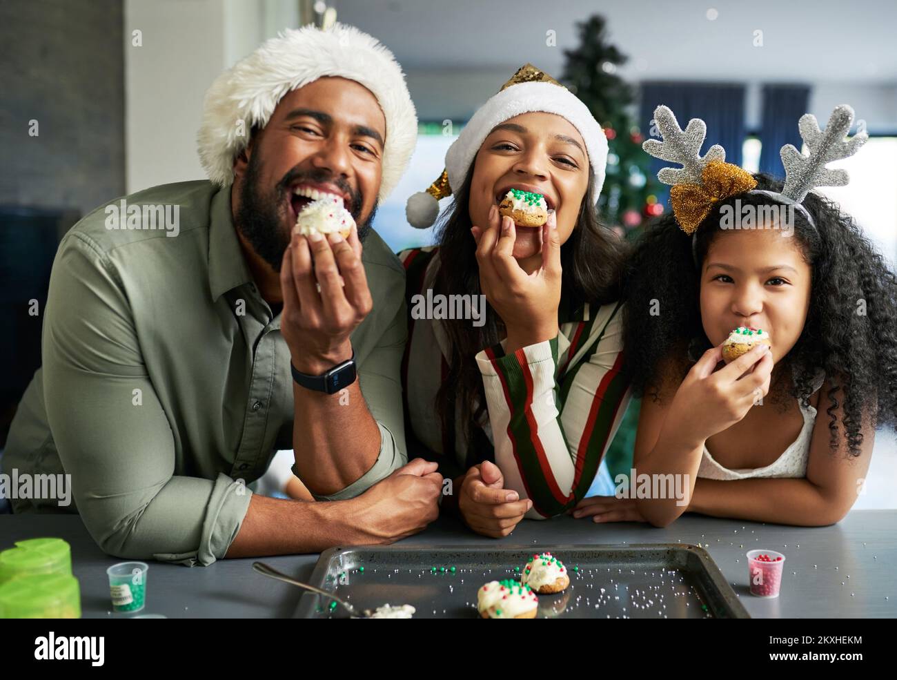 Christmas, family and cookie eating of a mother, father and girl in a home kitchen with happiness. Holiday baking, celebration and family home Stock Photo