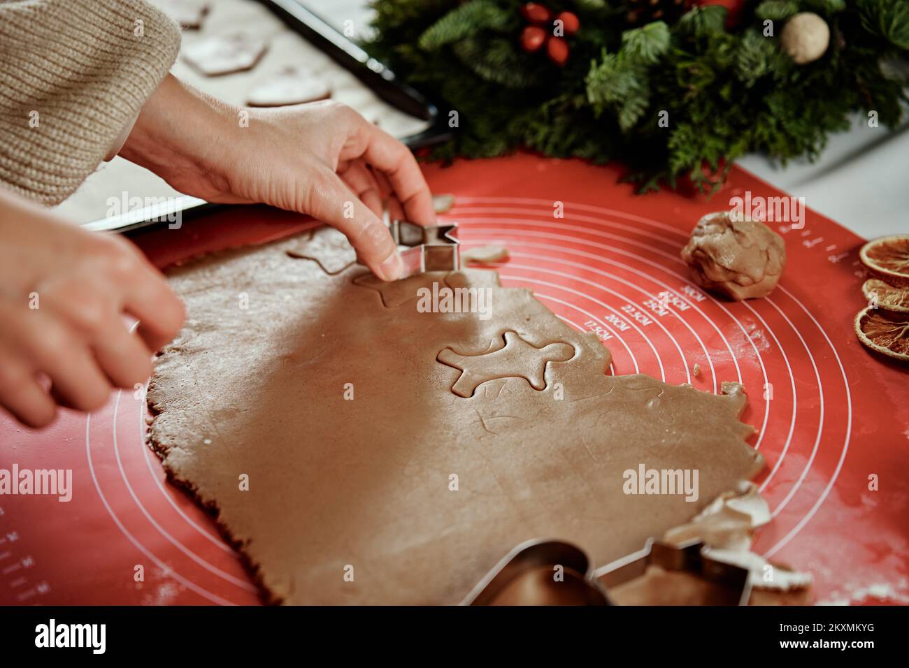 Woman preparing gingerbread cookies at kitchen with Christmas decorations. Female hands cutting ginger dough with cutter to making cookies for winter holidays Stock Photo
