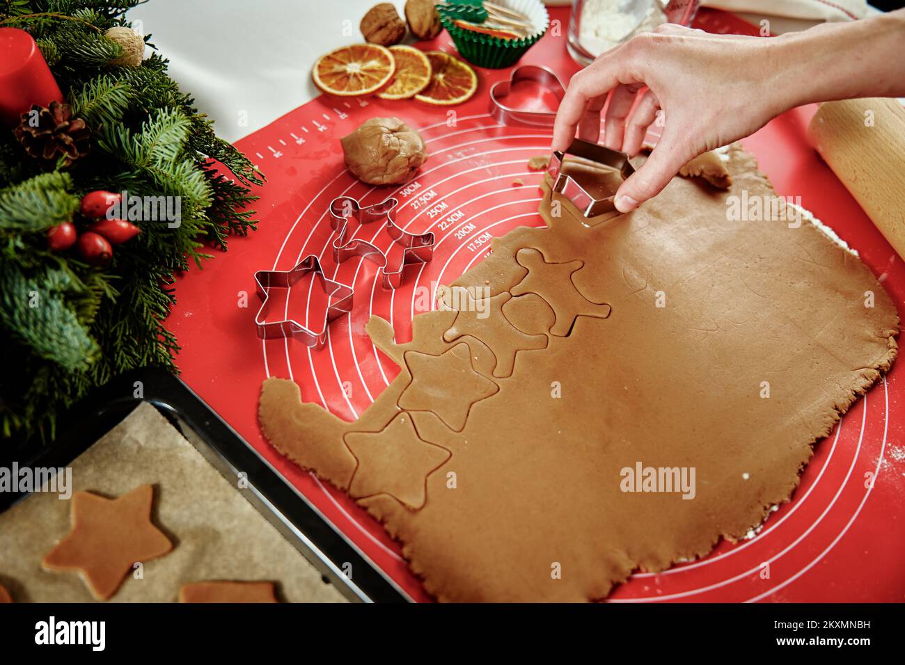 Woman preparing gingerbread cookies at kitchen with Christmas decorations. Female hands cutting ginger dough with cutter to making cookies for winter holidays Stock Photo