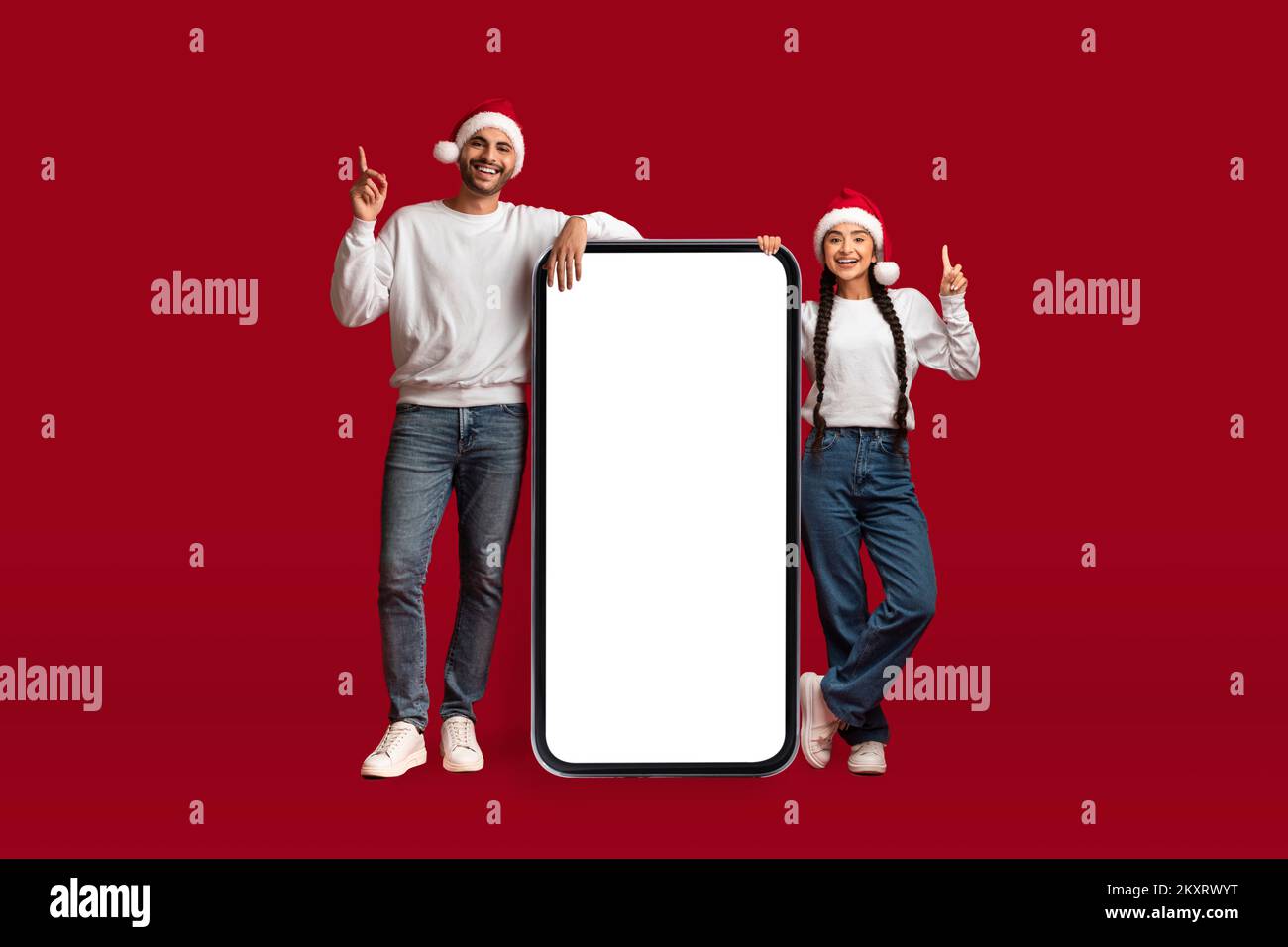Chistmas List. Happy Arab Couple Wearing Santa Hats Standing Near Blank Smartphone Stock Photo