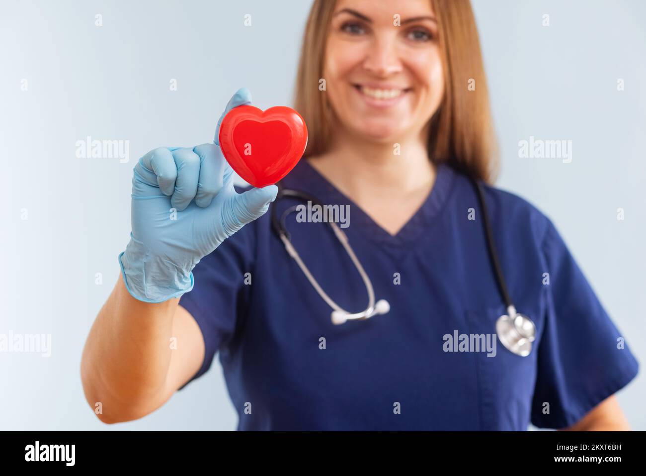Female doctor with stethoscope holding red heart on blue background ...