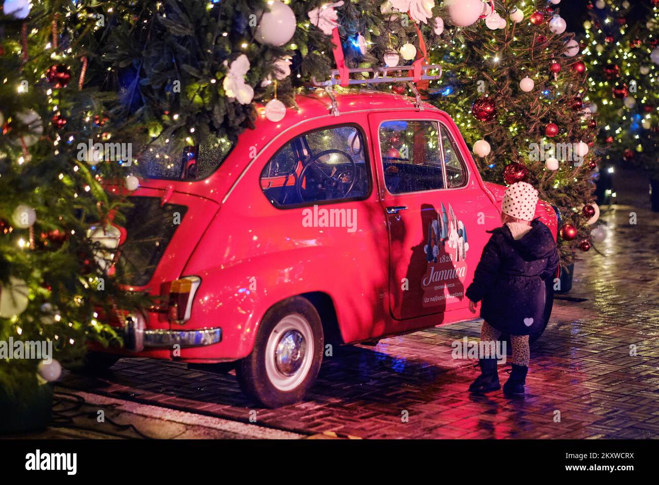 People taking photos by the little red Zastava 750 car, populary know as Fico with mounted giant Christmas tree on the roof during Advent time in Zagreb, Croatia on 01. December, 2021. Photo: Tomislav Miletic/PIXSELL Stock Photo