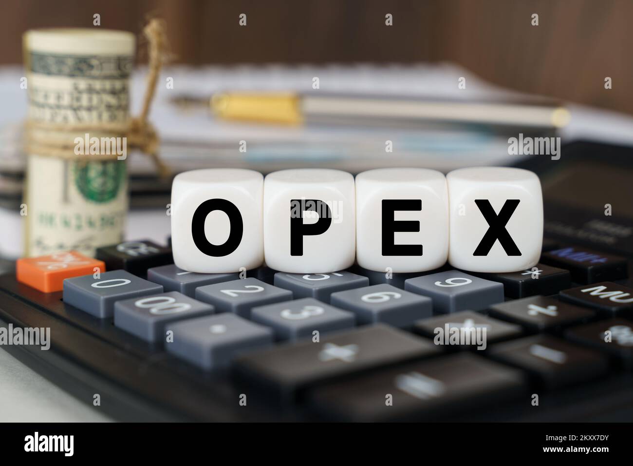 Business and finance concept. There are cubes on the calculator that say - OPEX. Nearby out of focus - dollars, notebook and pen Stock Photo