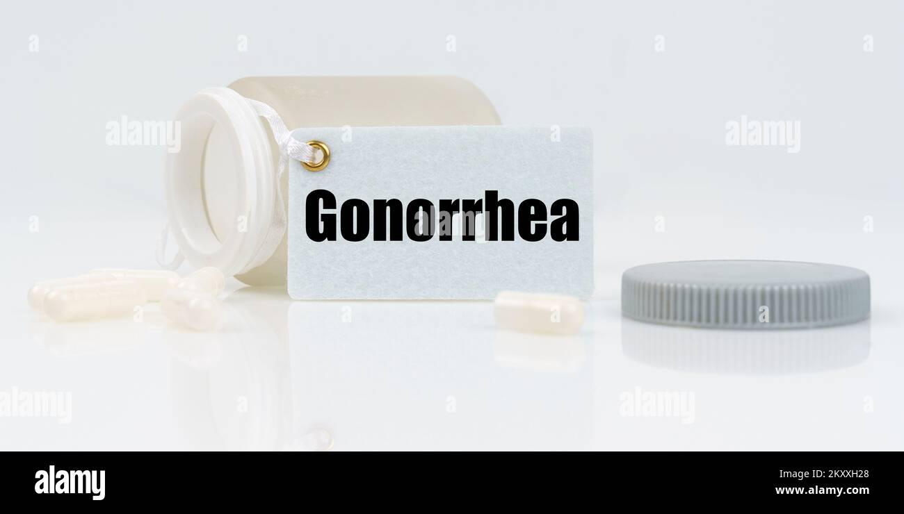 Medicine and health concept. On a white reflective background, there are pills and a jar of drugs with a tag that says - Gonorrhea Stock Photo