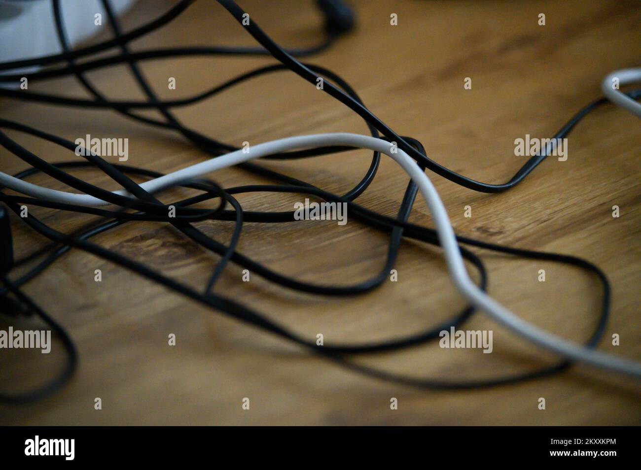 Cable chaos clutter from multiple electric wire extension cords and multi-contact plugs on wooden floor or table background Stock Photo