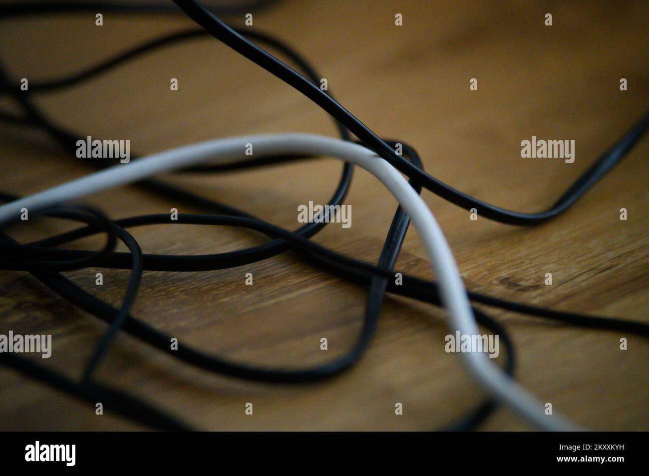 Cable chaos clutter from multiple electric wire extension cords and multi-contact plugs on wooden floor or table background Stock Photo