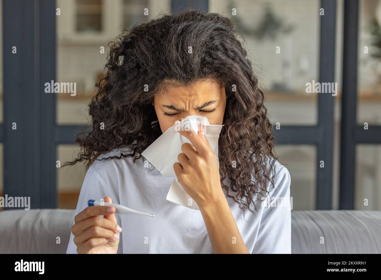 African American woman is very sick measures temperature, feels very bad. Young ill female blows his nose in a napkin Stock Photo