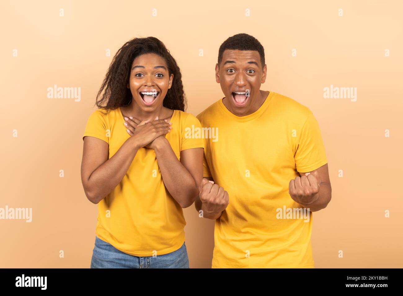 Wow, yes. Overjoyed black man and woman cheering and shaking clenched fists, looking at camera in excitement Stock Photo