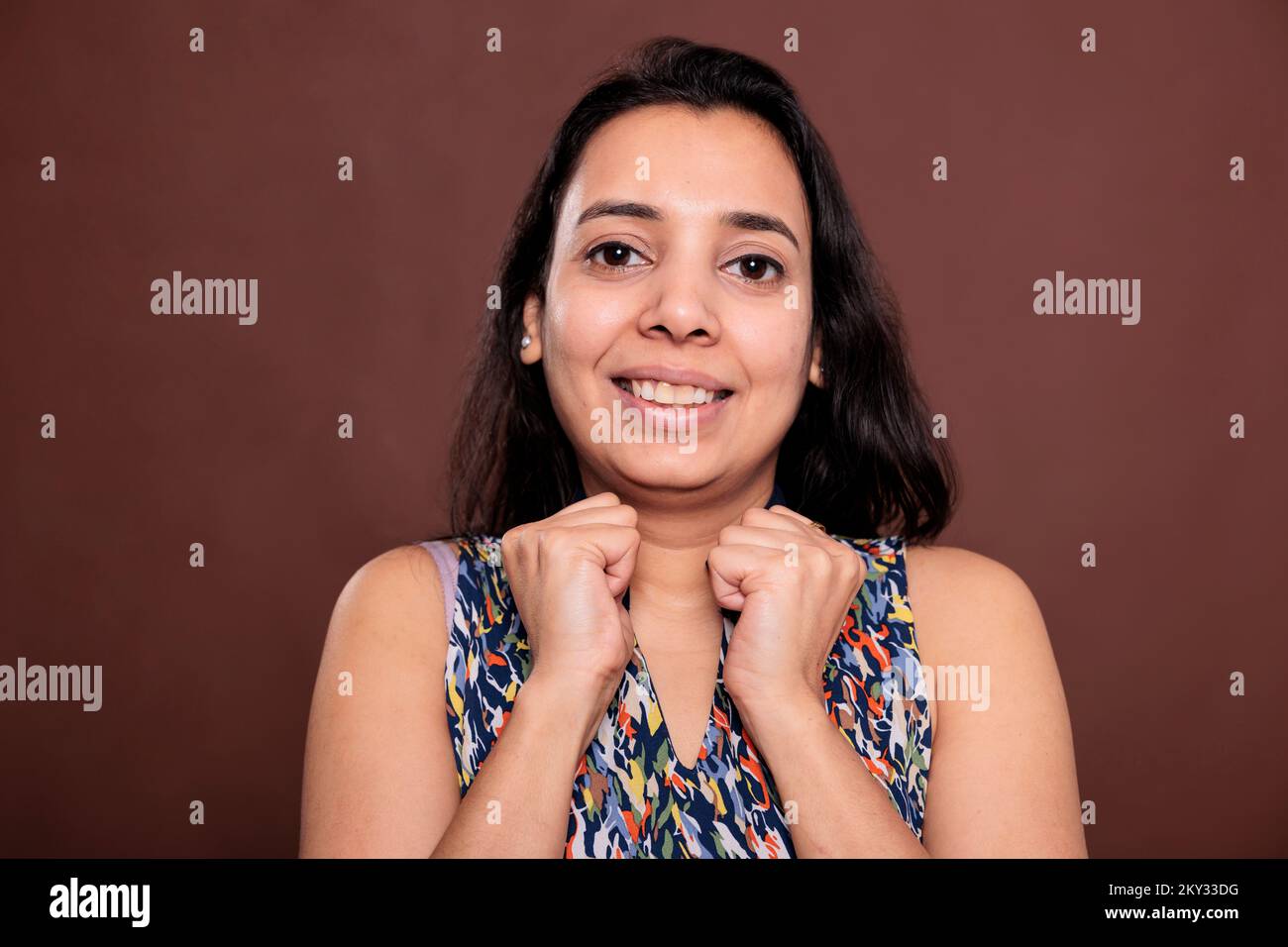 Smiling indian woman with clenched fists near cheeks medium close up