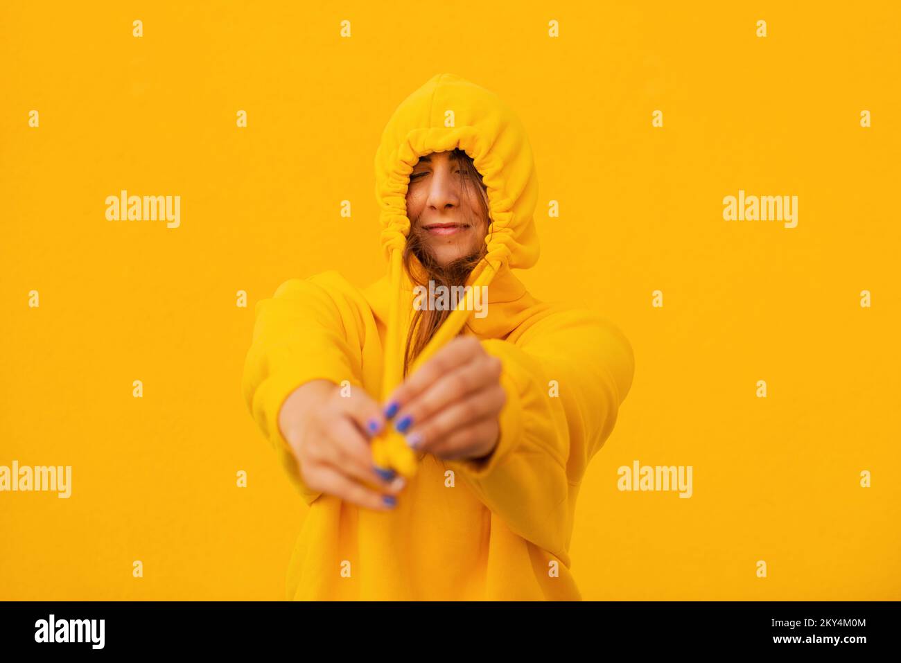 Cheerful casual young woman in a yellow hoodie is having fun on a colorful yellow background Stock Photo