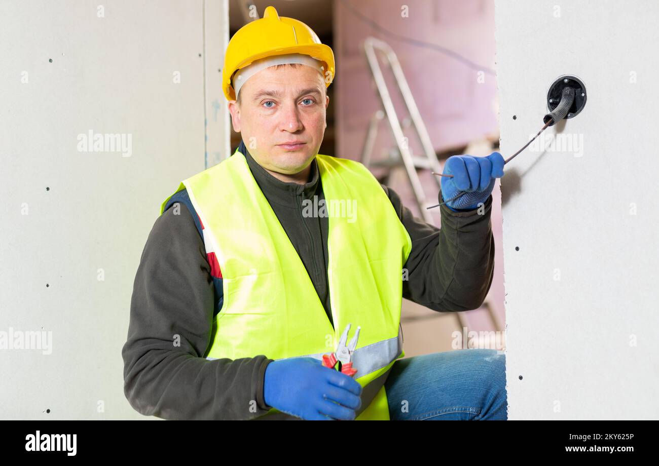Experienced electrician laying electric wires in building under ...