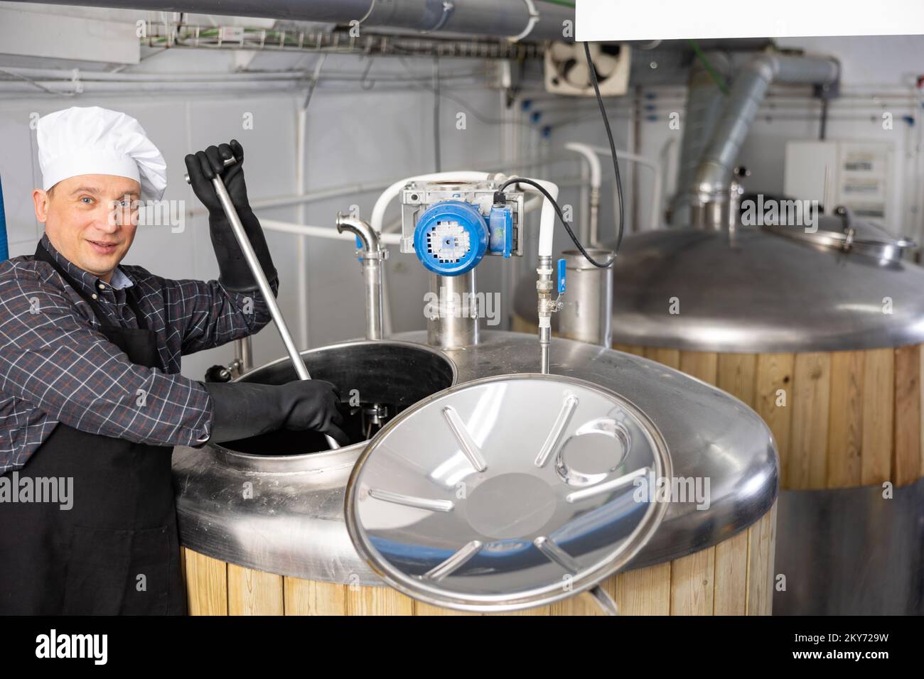 Skilled brewer mixing raw materials in fermentation vessel in brewery