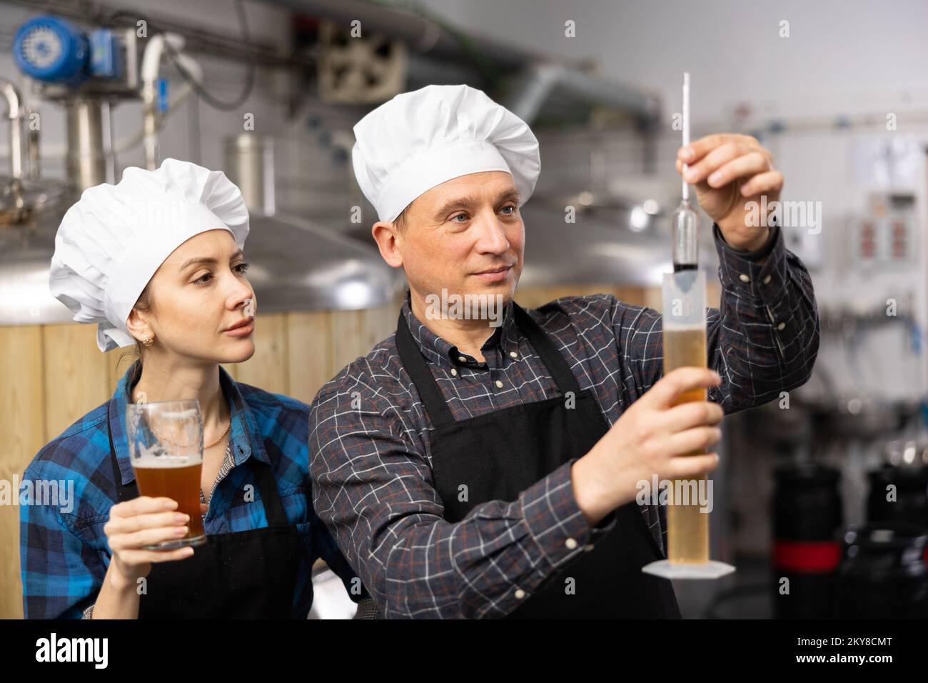 Man and woman brewmasters measuring beer with alcoholometer Stock Photo