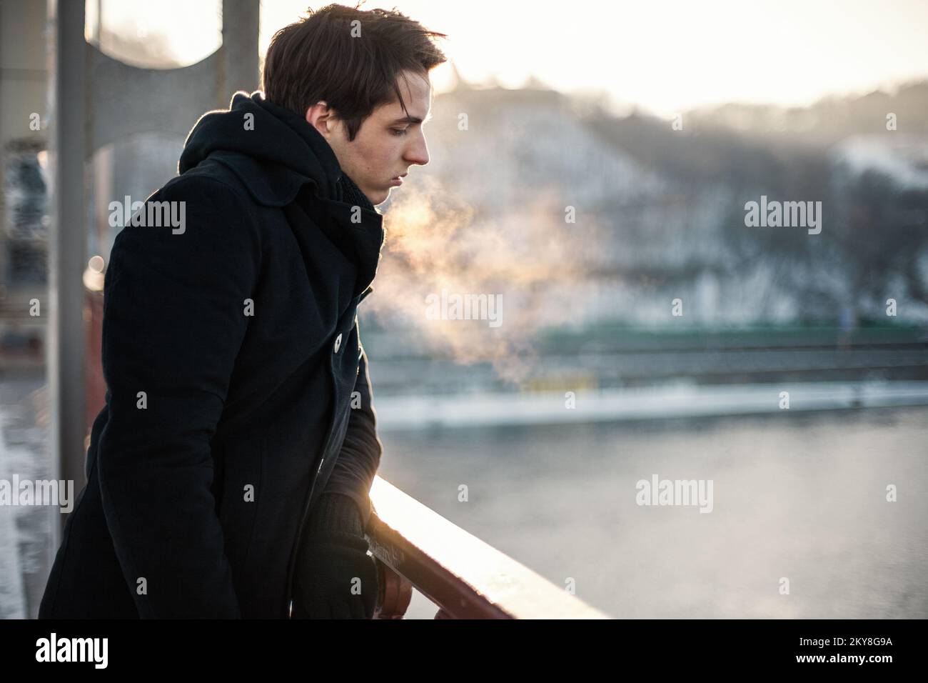 Thoughtful hipster guy standing on the bridge looking down on the river Stock Photo