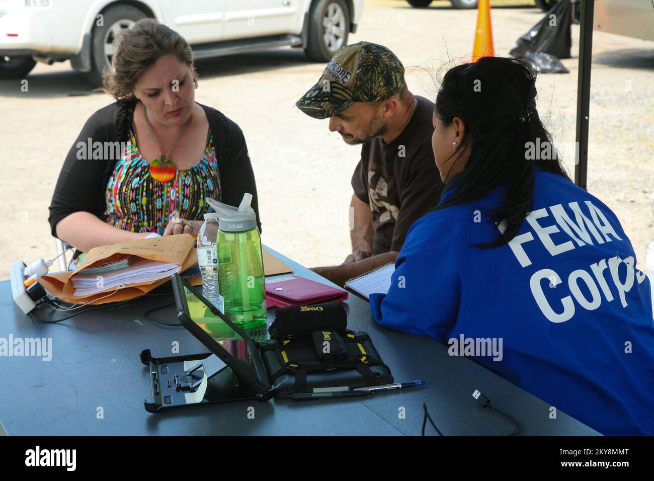 Mayflower, AR, May 7, 2014 â€“ Charlotte Leher (left) and Vernon Carlson (center), disaster survivors affected by the severe storms and tornado that impacted much of the Mayflower community on April 27, seek help from FEMA Corps Alpine 2 team member Cassandara Ly (right) at a Mobile Registration Intake Center (MRIC). FEMA assists individuals and their families and supports state, local and tribal governments in their recovery efforts following a natural disaster. Arkansas Severe Storms, Tornadoes, and Flooding. Photographs Relating to Disasters and Emergency Management Programs, Activities, an Stock Photo