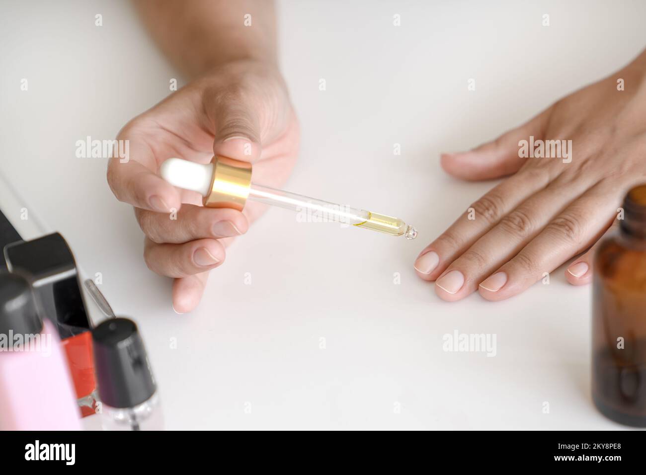 Woman holds pipette with oil to apply to her nails for treatment and