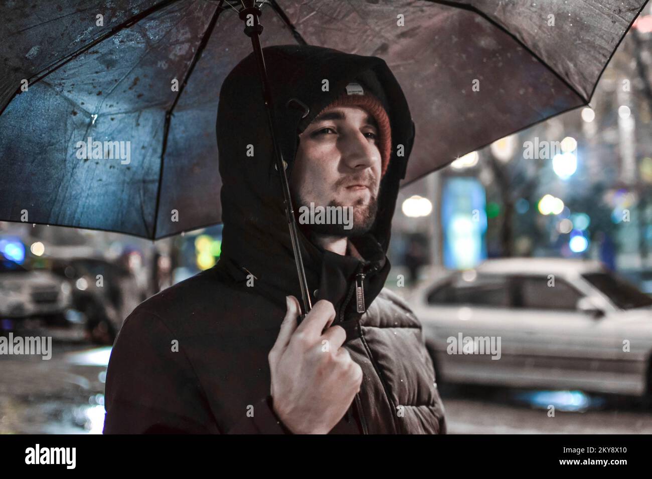 Young thoughtful upset man under umbrella at night. Bad weather Stock Photo